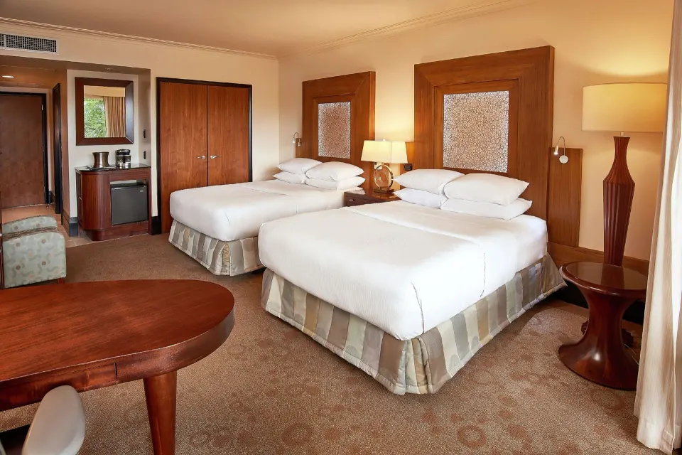 Two-bed Deluxe Pool View room at Hilton Trinidad & Conference Centre with wood furnishings and lamps.