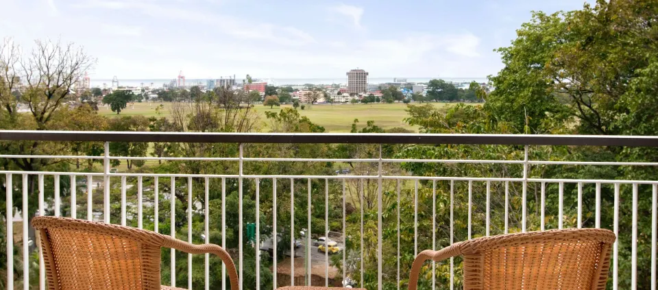 Deluxe Room balcony with wicker chairs and city view at Hilton Trinidad & Conference Centre.