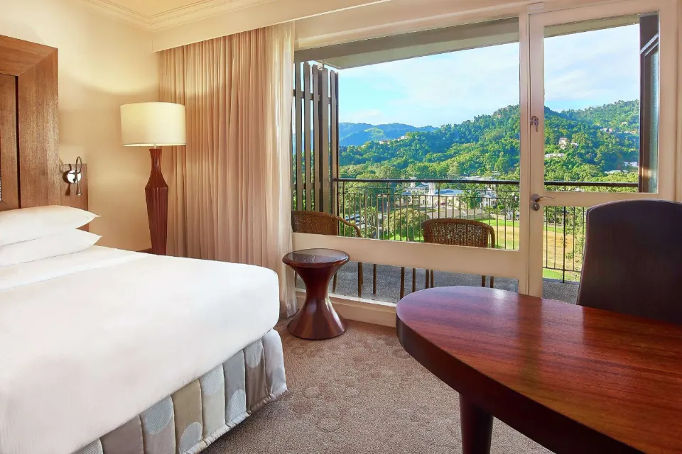 Deluxe Room king bed and desk beside balcony doors at Hilton Trinidad & Conference Centre.