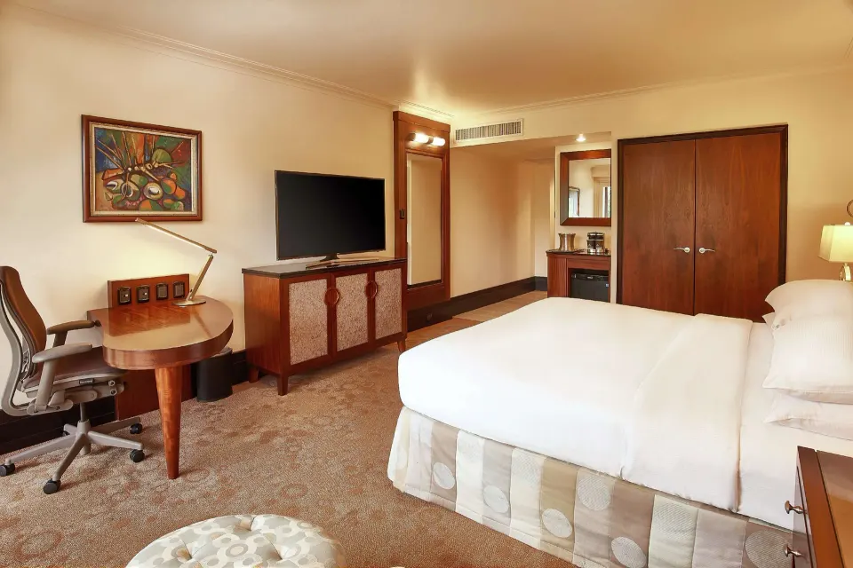 Deluxe Room king bed with desk, TV, and wardrobe at Hilton Trinidad & Conference Centre.