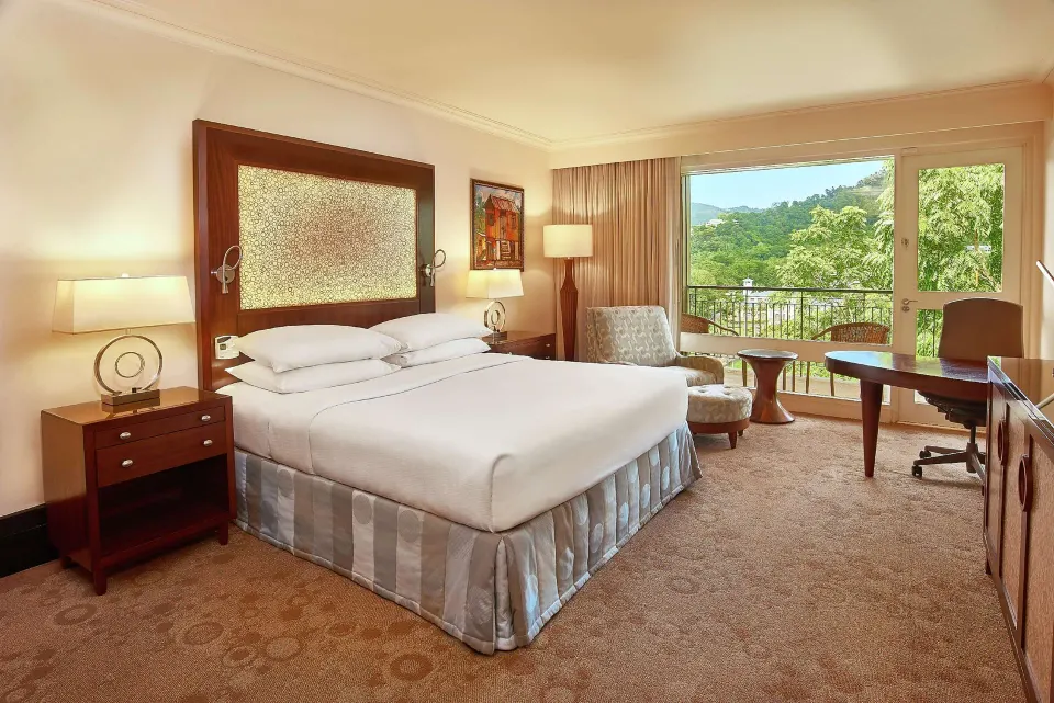 Deluxe Room king bed with lounge chair and balcony at Hilton Trinidad & Conference Centre.