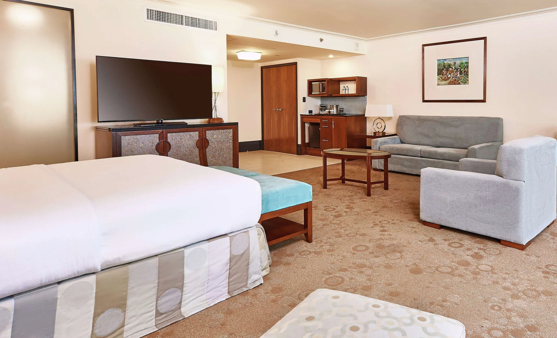 Deluxe Studio Suite with king bed, sofa, TV, and kitchenette at Hilton Trinidad & Conference Centre.