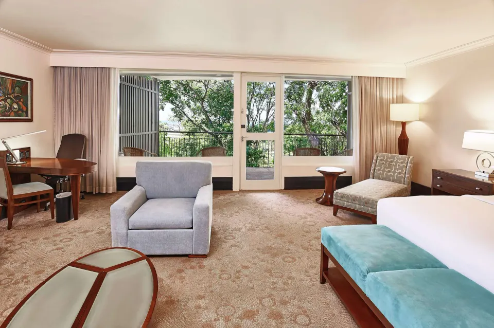 Deluxe Studio Suite with king bed, desk, seating, and balcony doors at Hilton Trinidad & Conference Centre.