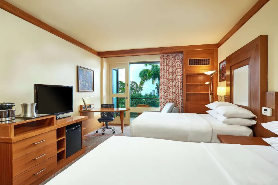 Executive Room with two beds, TV, desk, and balcony at Hilton Trinidad & Conference Centre.