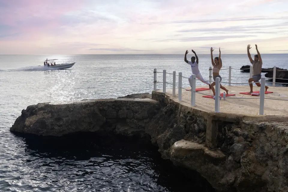 Guests practice yoga on a rocky ocean platform at HM Alma de Bayahibe.