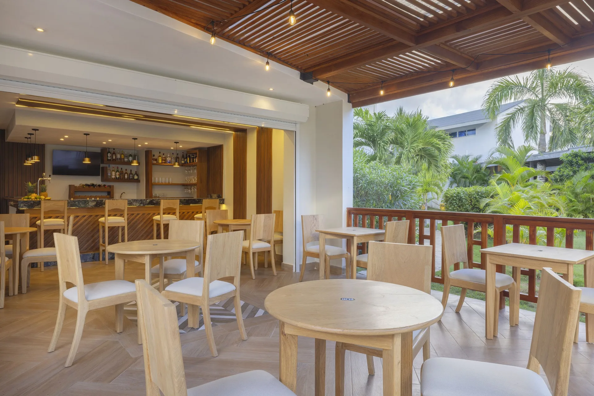 Covered terrace tables beside a bar and tropical landscaping at HM Alma de Bayahibe.