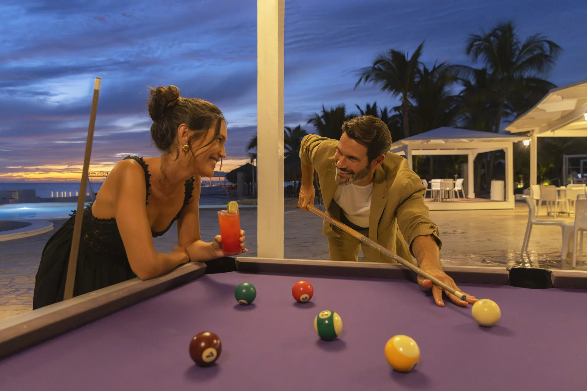 Guests play pool outdoors at dusk with a cocktail at HM Alma de Bayahibe.