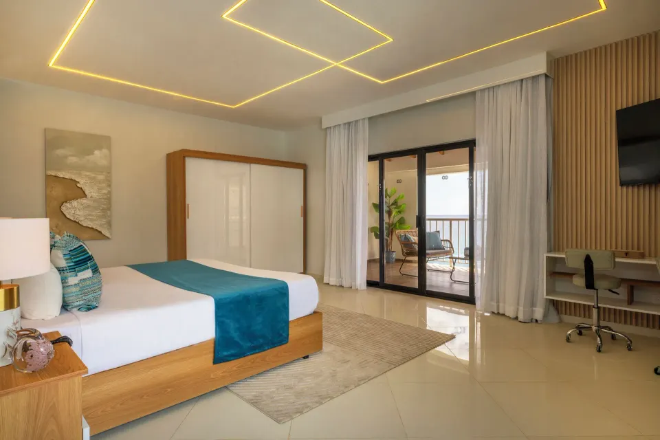Junior Suite king bed, wardrobe, desk and balcony doors at HM Alma de Bayahibe.
