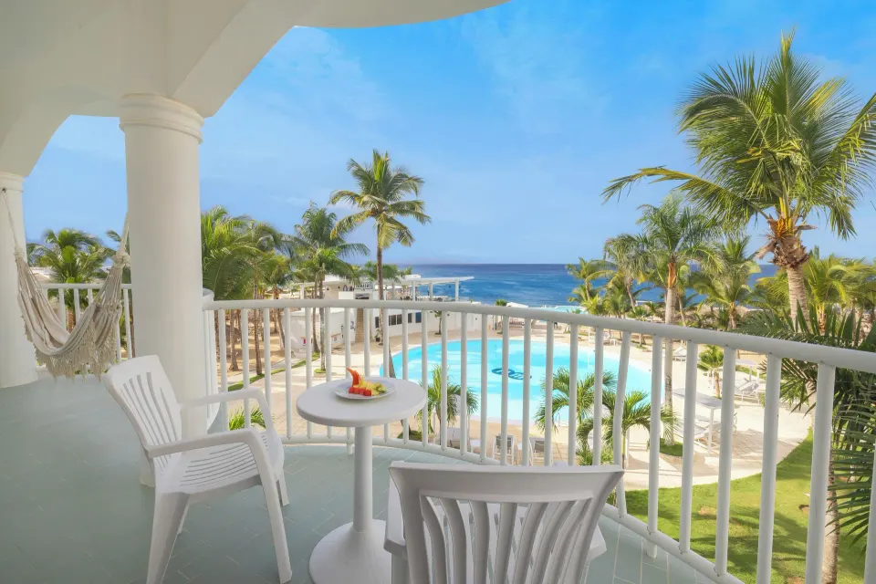 Sea View room balcony with chairs, hammock, pool, palms, and ocean at HM Alma de Bayahibe.