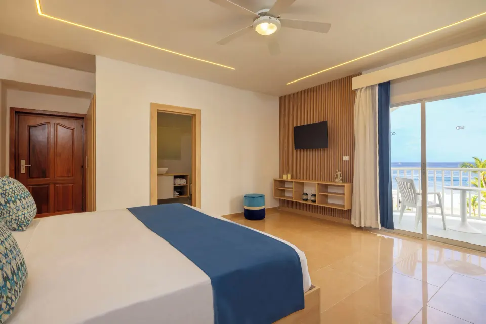 Sea View room with bed, TV wall, balcony chairs, and ocean beyond at HM Alma de Bayahibe.