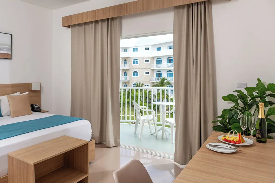 Guest room with bed, desk and balcony seating at HM Alma de Bayahibe.