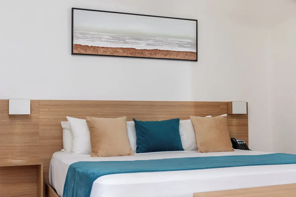 King bed with teal runner, pillows and wall art at HM Alma de Bayahibe.