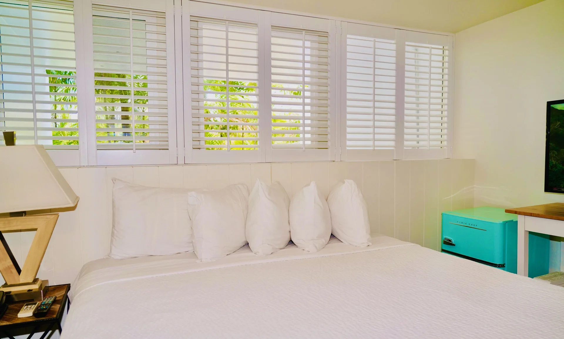 Guest room bed with white shutters and turquoise mini fridge at Hotel La Croix.