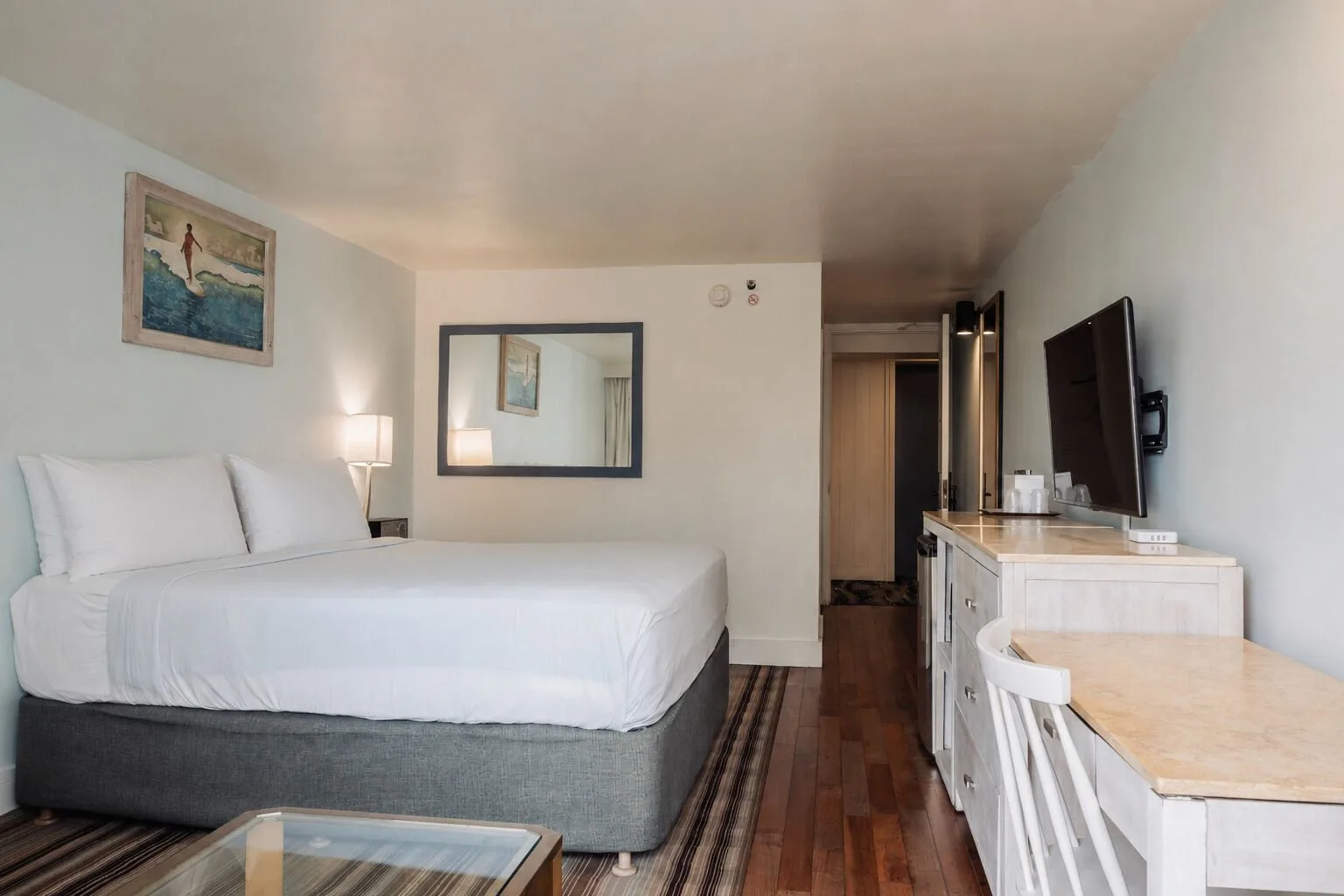 Ali'i Waikiki king room at Hotel La Croix with a bed, dresser, desk, wall mirror, and mounted TV.