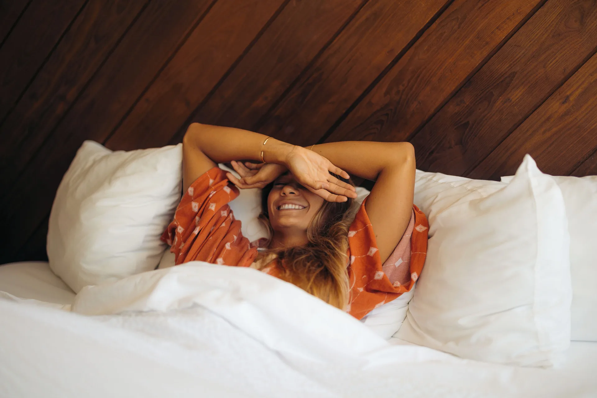 Guest smiling in white bedding against a wood headboard at Hotel La Croix.