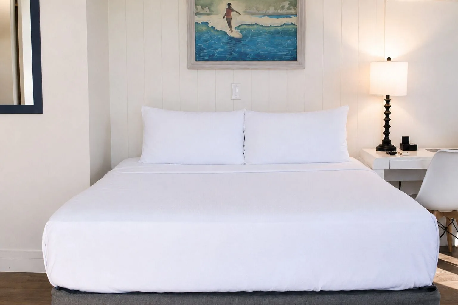 White king bed with surf artwork and bedside lamp in Penthouse Hoku Terrace at Hotel La Croix.