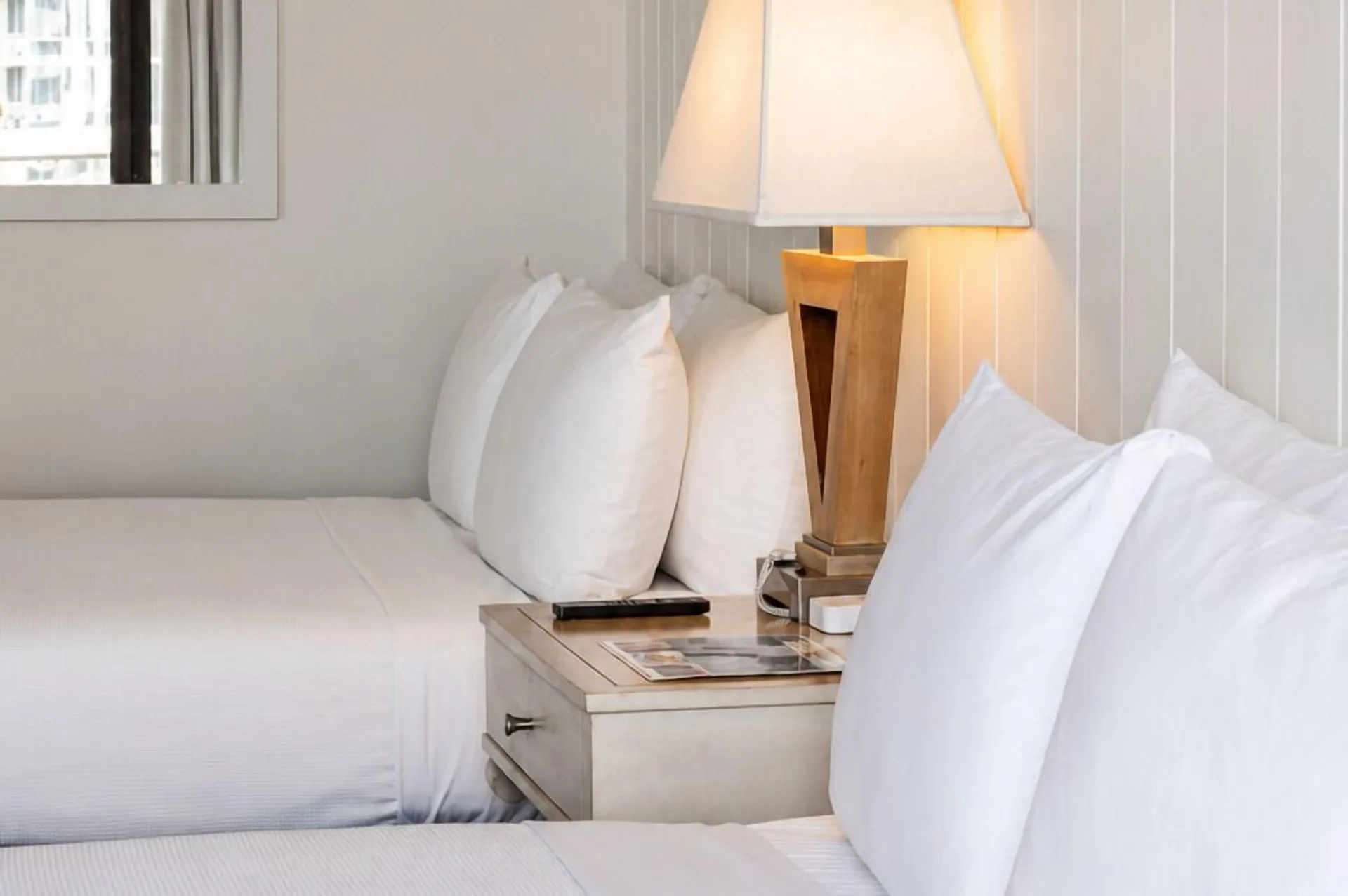 Two white beds with pillows and a lit bedside lamp in a Hotel La Croix guest room.