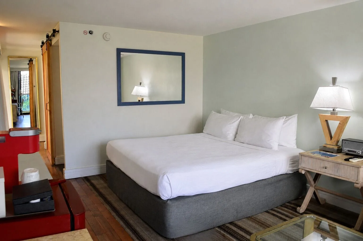King bed and red mini fridge in a Premium Kalakaua Haus Corner Two Lanai room at Hotel La Croix.