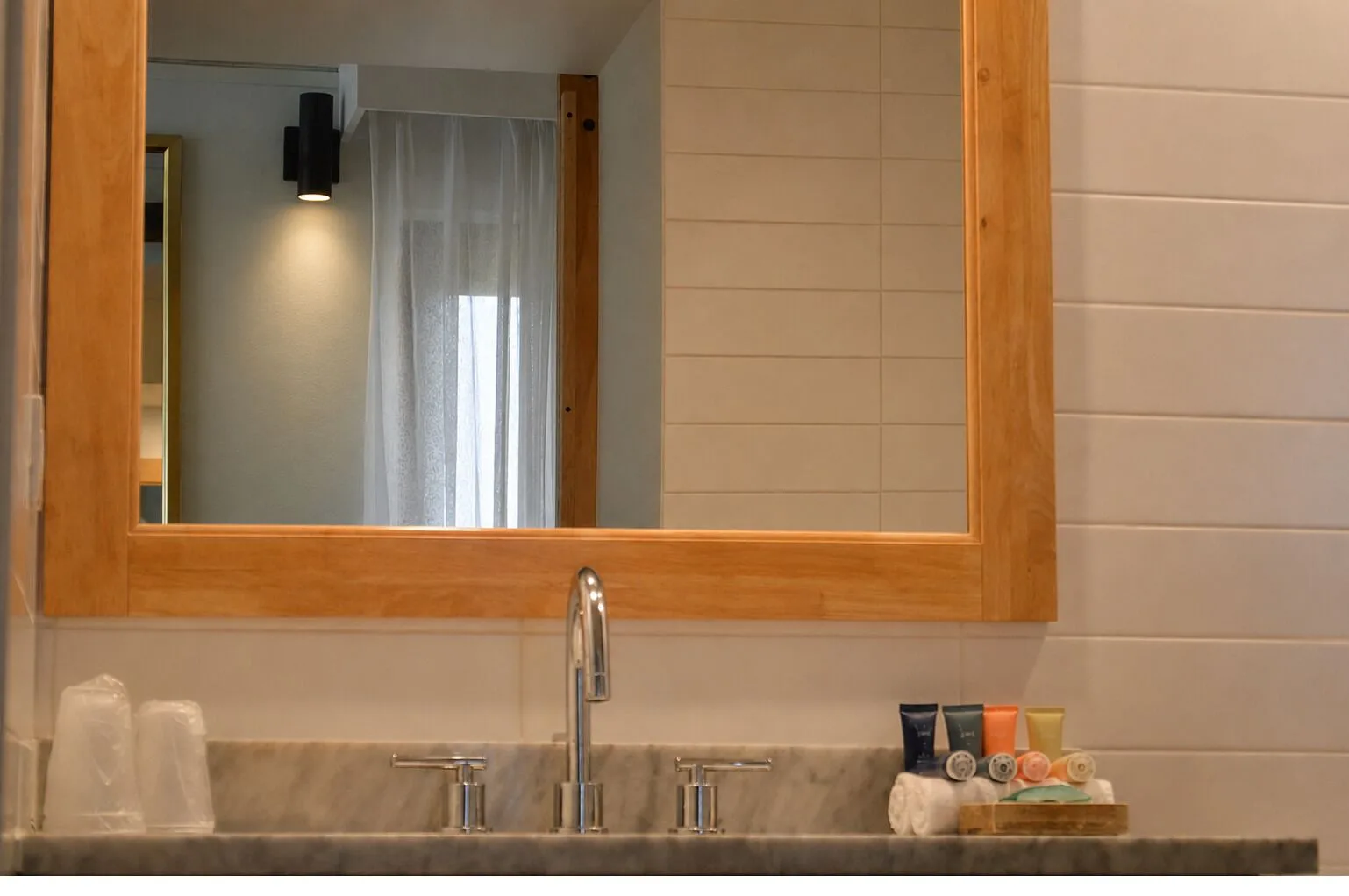 Bathroom mirror, sink, cups, and bath amenities in a guest room at Hotel La Croix.