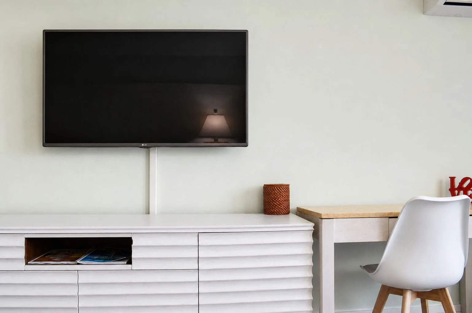 Wall-mounted TV, dresser, and desk in a Premium Kalakaua Haus room at Hotel La Croix.