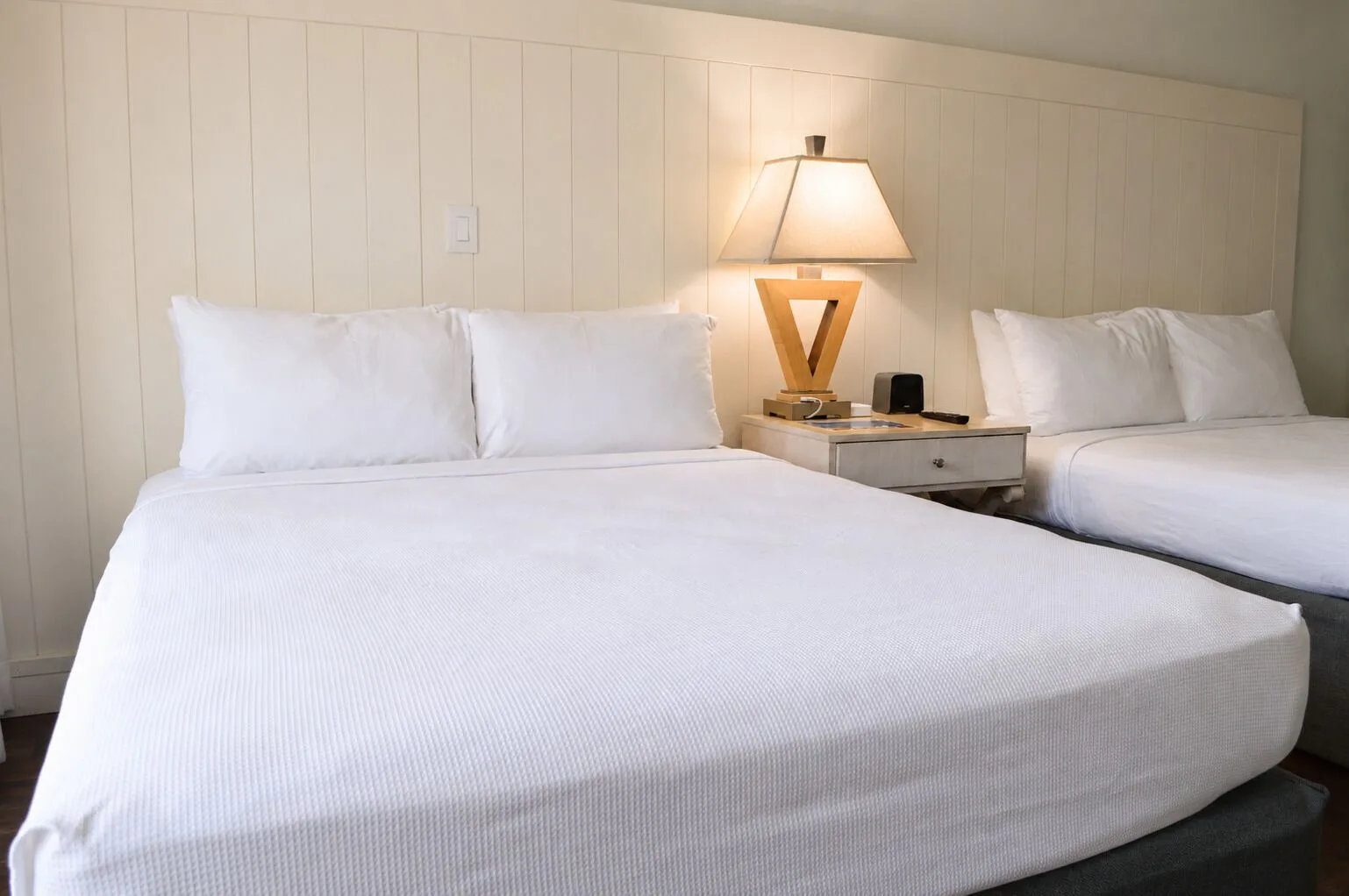 Two white beds with a shared nightstand in a Premium Kalakaua Haus room at Hotel La Croix.