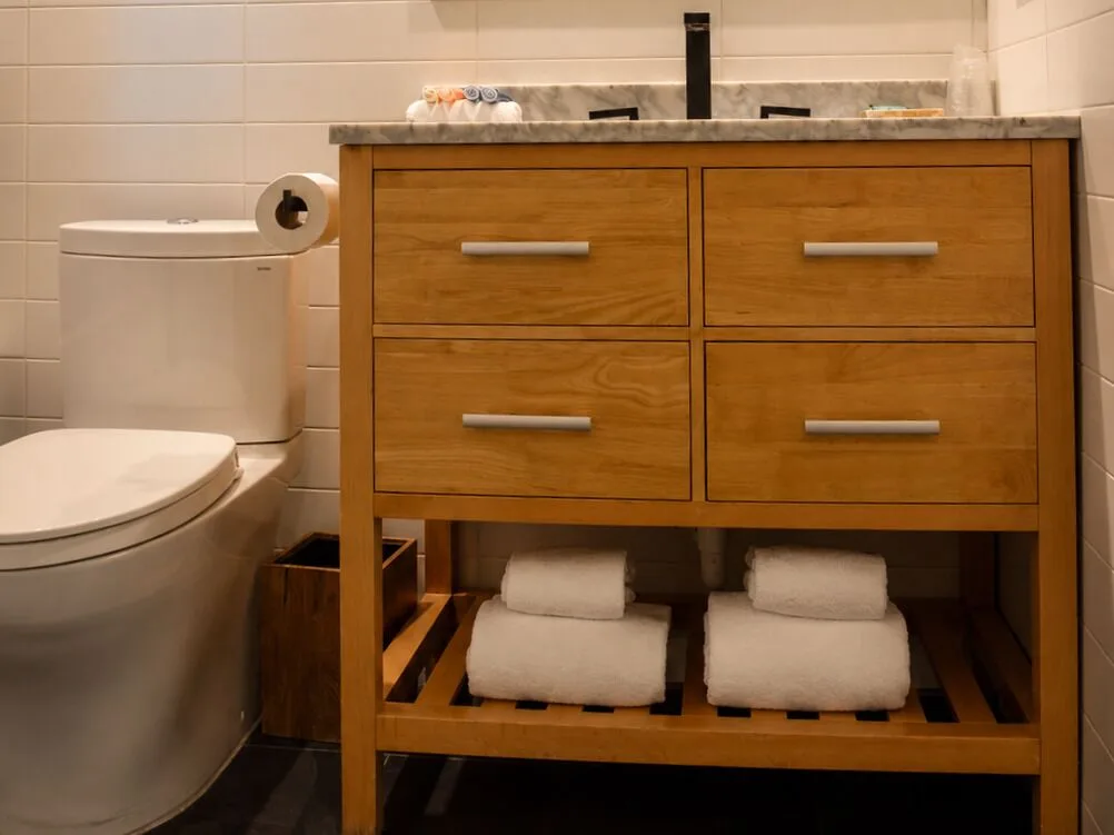 Wood vanity, towels, and toilet in a Premium Kalakaua Haus bathroom at Hotel La Croix.