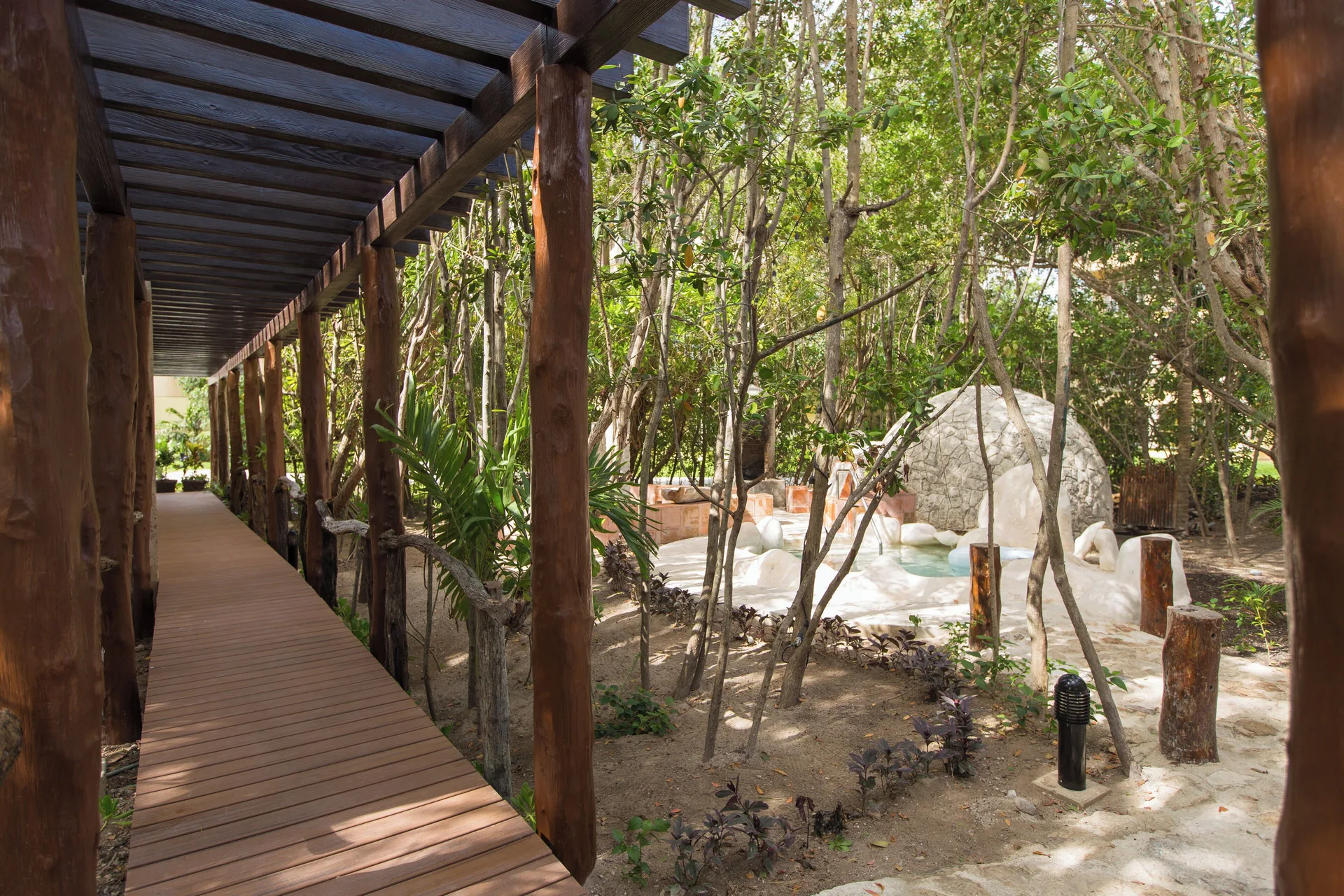 A covered wooden walkway passes through garden spa grounds at Hotel Marina El Cid Spa & Beach Resort.