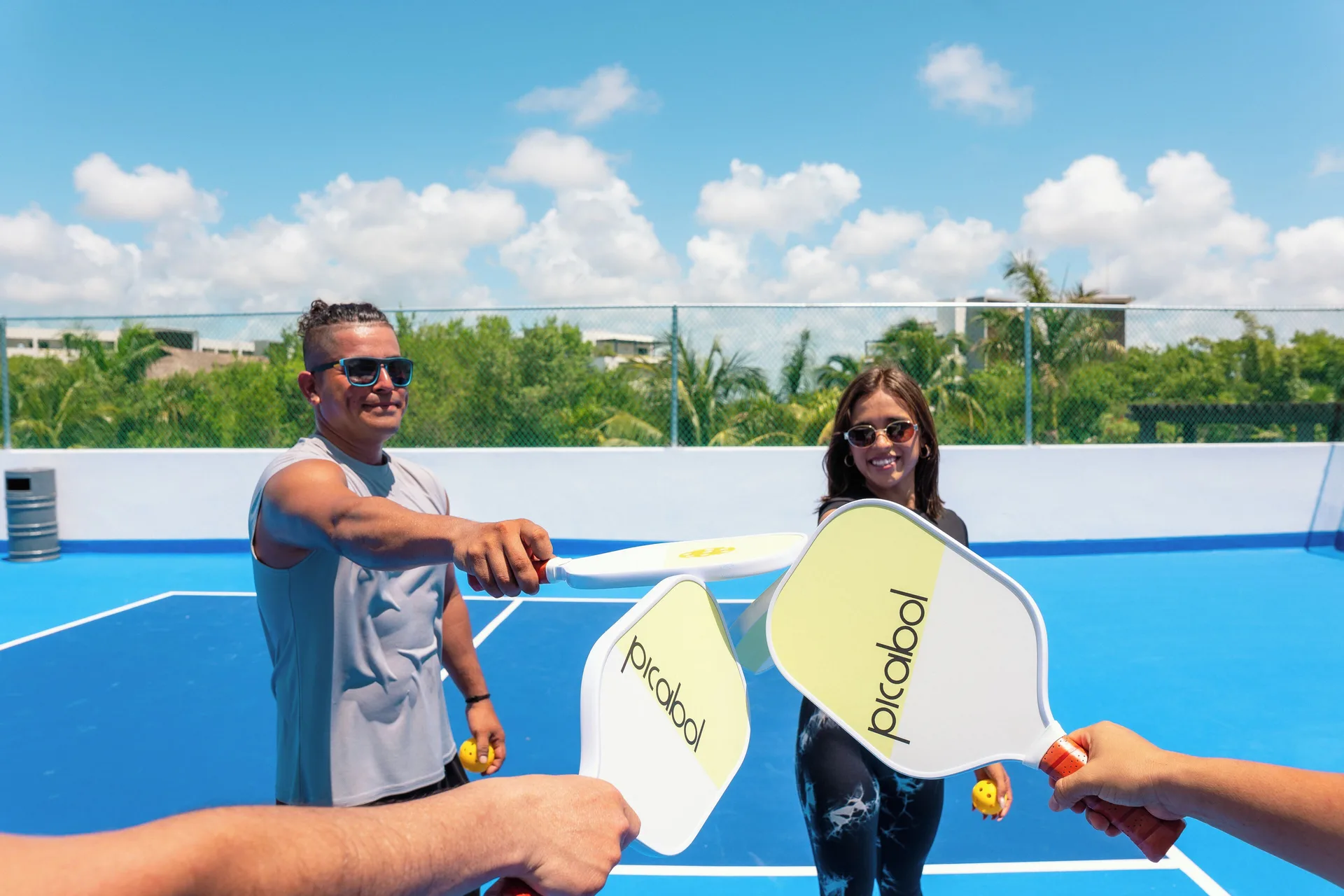 Group holding pickleball paddles on a blue court at Hotel Marina El Cid Spa & Beach Resort.
