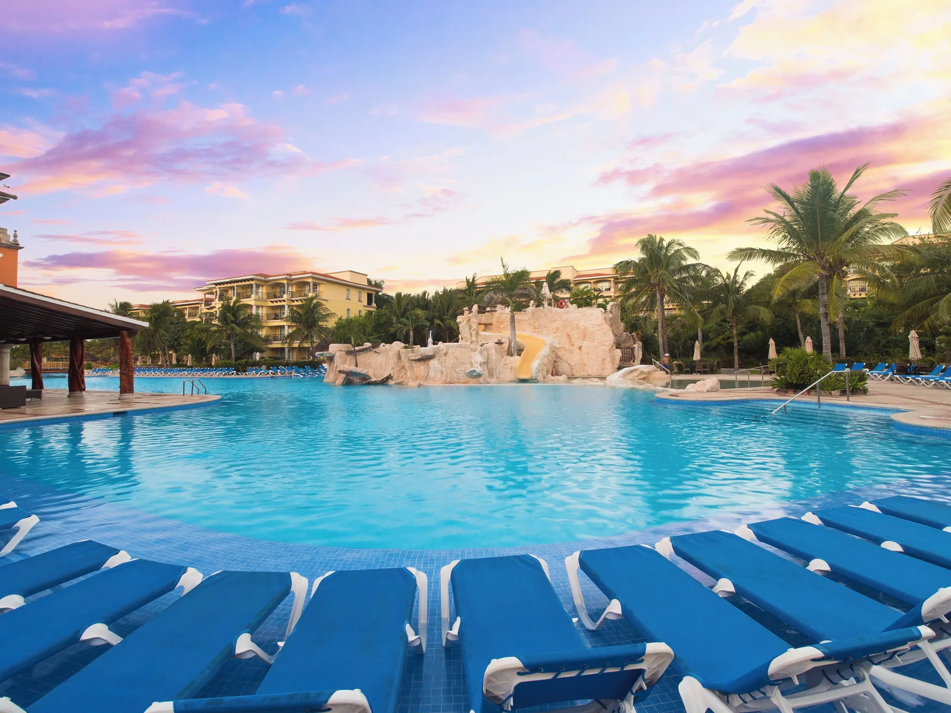 Pool with blue loungers and rock waterfall at Hotel Marina El Cid Spa & Beach Resort.