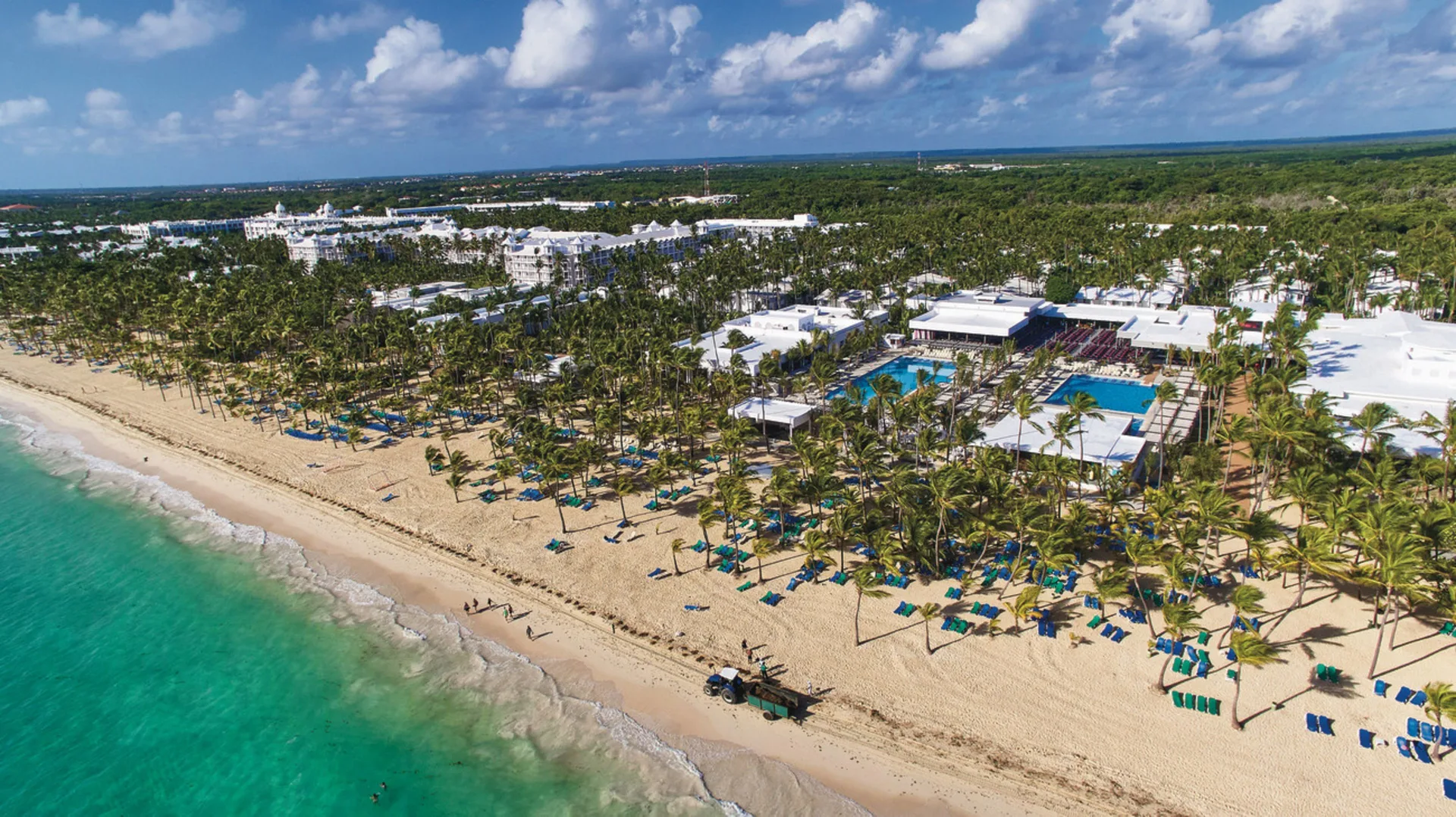 Aerial view of Hotel Riu Bambu along a palm-lined beach with pools and turquoise water.