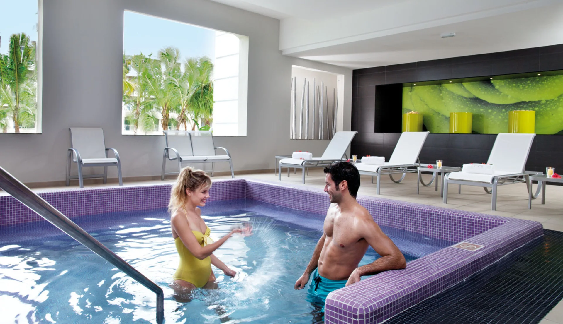 Indoor spa pool with loungers and palm views at the Renova Spa serving Hotel Riu Bambu guests.