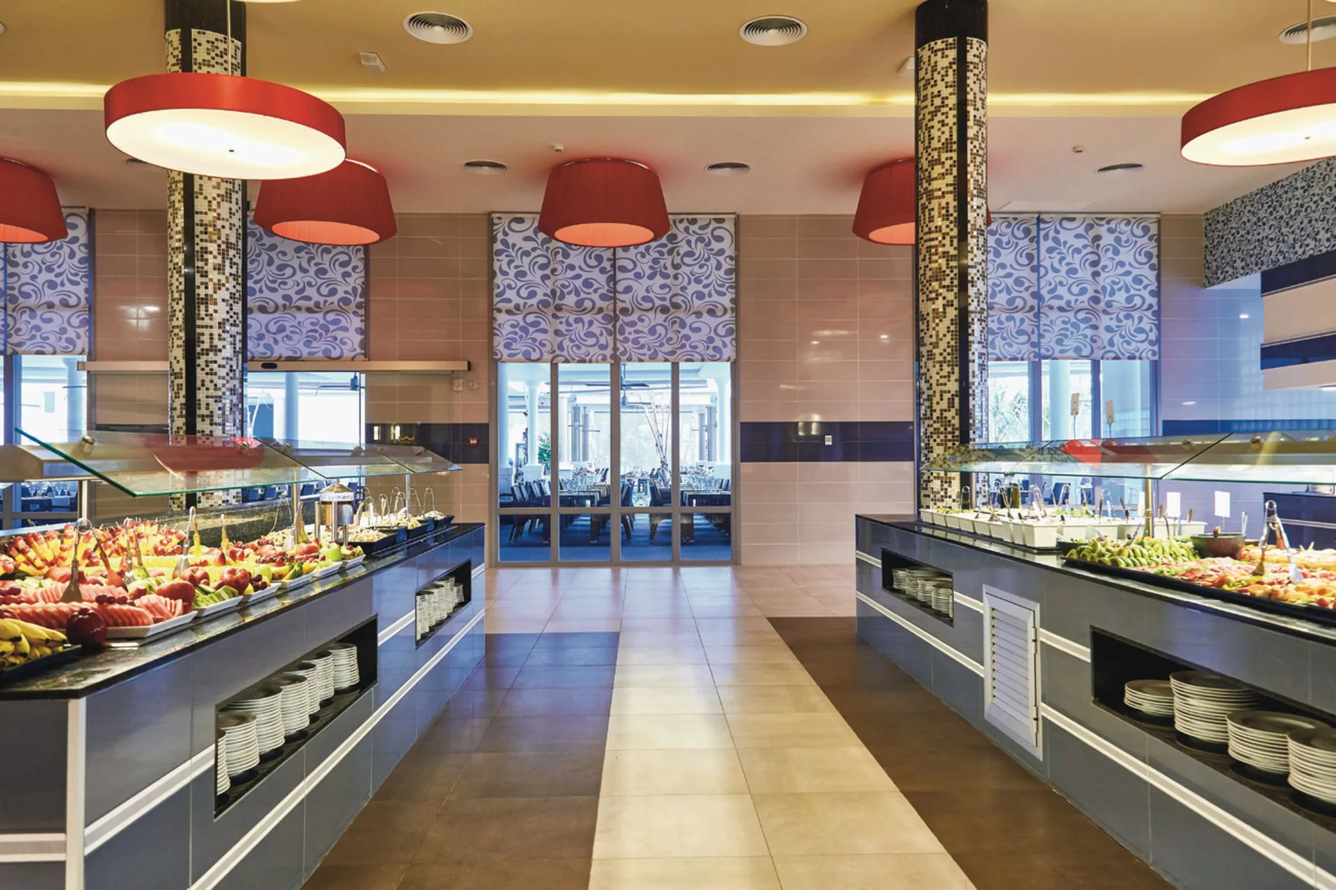 Buffet stations with fruit and cold dishes line a dining room at Hotel Riu Bambu.