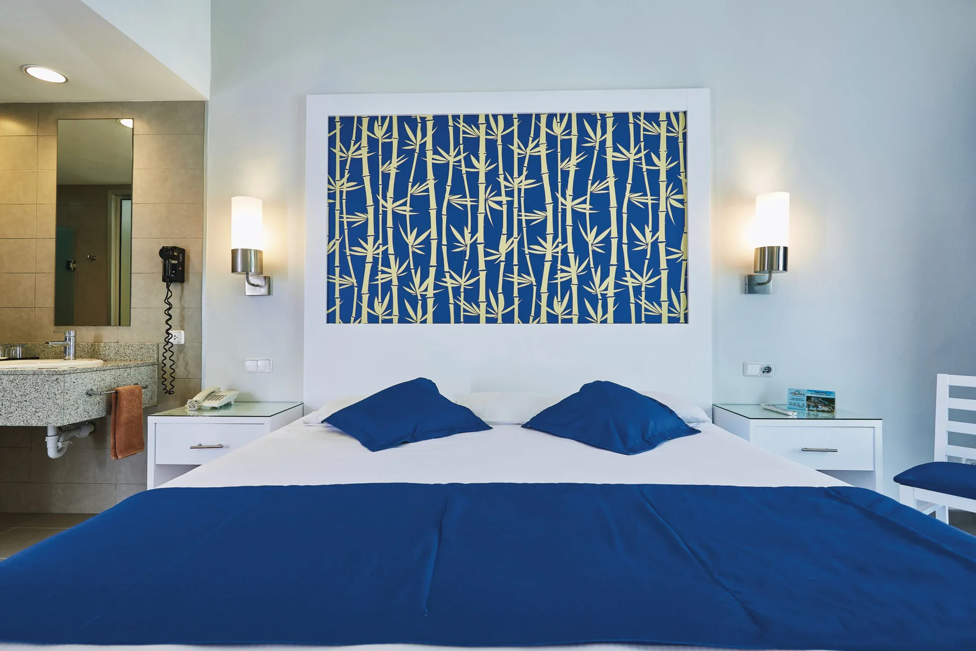 Deluxe Room bed with blue accents and open vanity area at Hotel Riu Bambu.