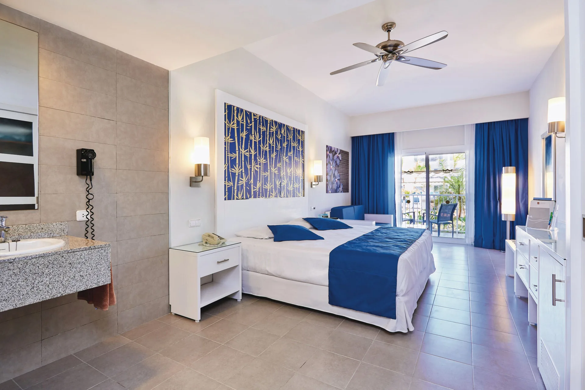 Family Room with bed, vanity, and balcony doors at Hotel Riu Bambu.