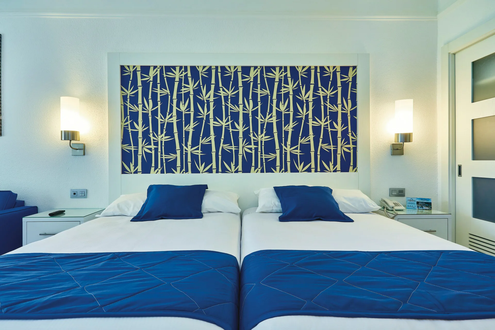 Family Room twin beds with blue bedding and bamboo-pattern wall art at Hotel Riu Bambu.