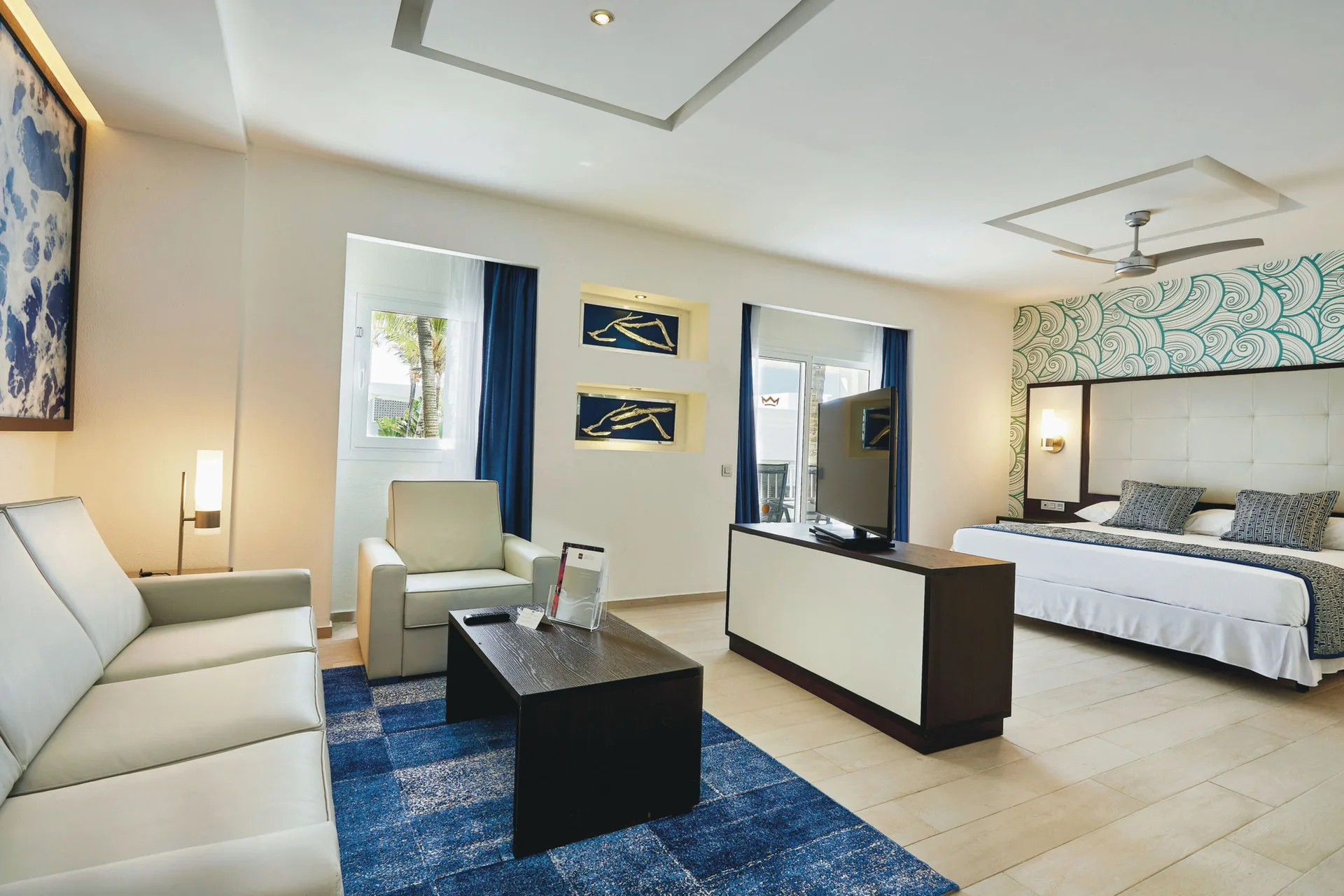 Junior Suite lounge area with sofa, armchair, coffee table and bed at Hotel Riu Bambu.