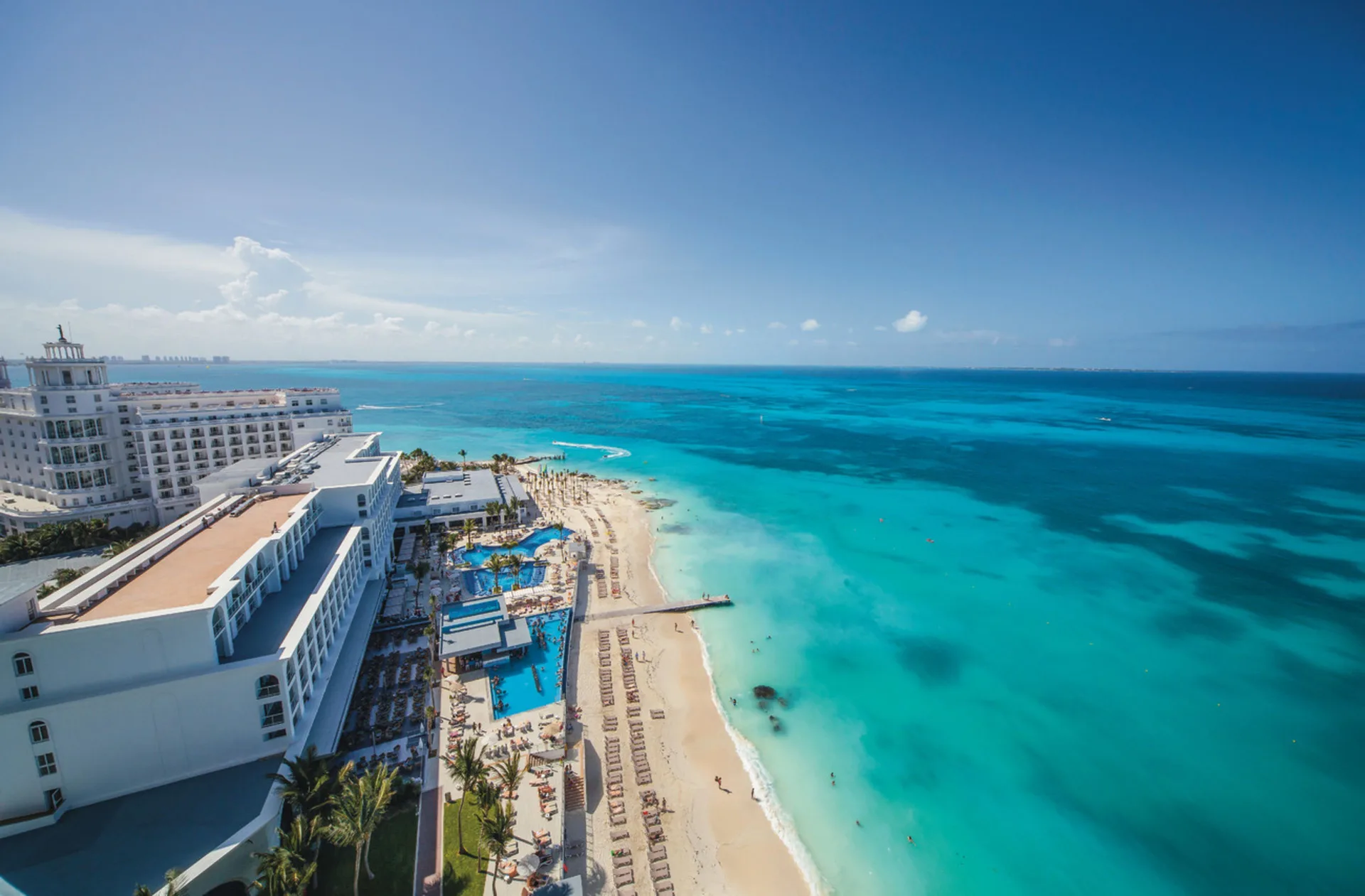 Aerial view of the beach, pools, and turquoise shoreline at Hotel Riu Cancun.