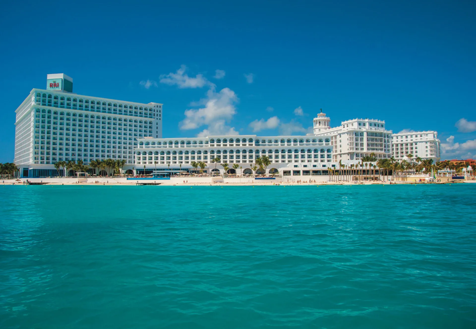 White beachfront resort buildings seen across turquoise water at Hotel Riu Cancun.