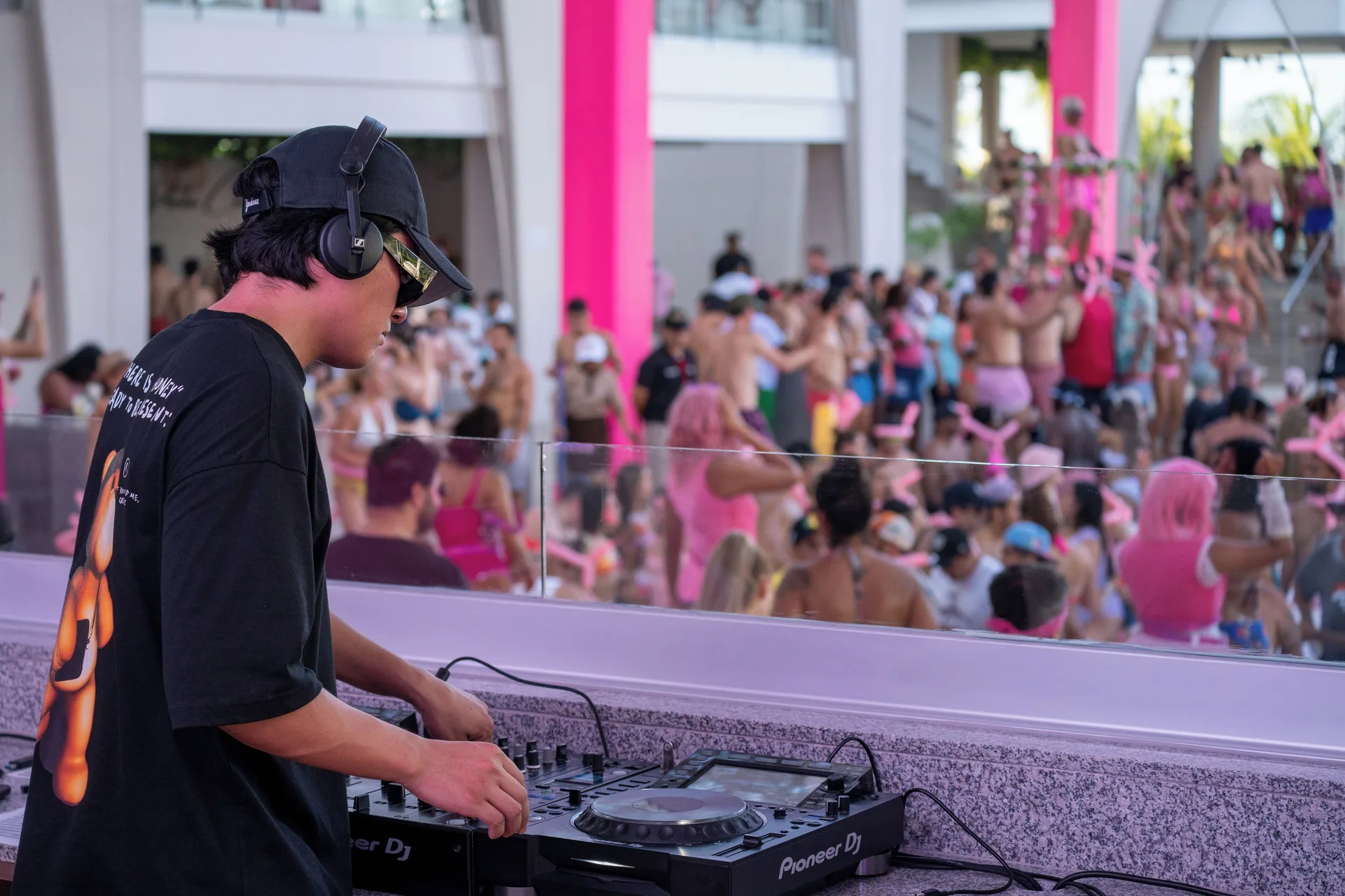 A DJ performs above a crowded pink-themed pool party at Hotel Riu Cancun.