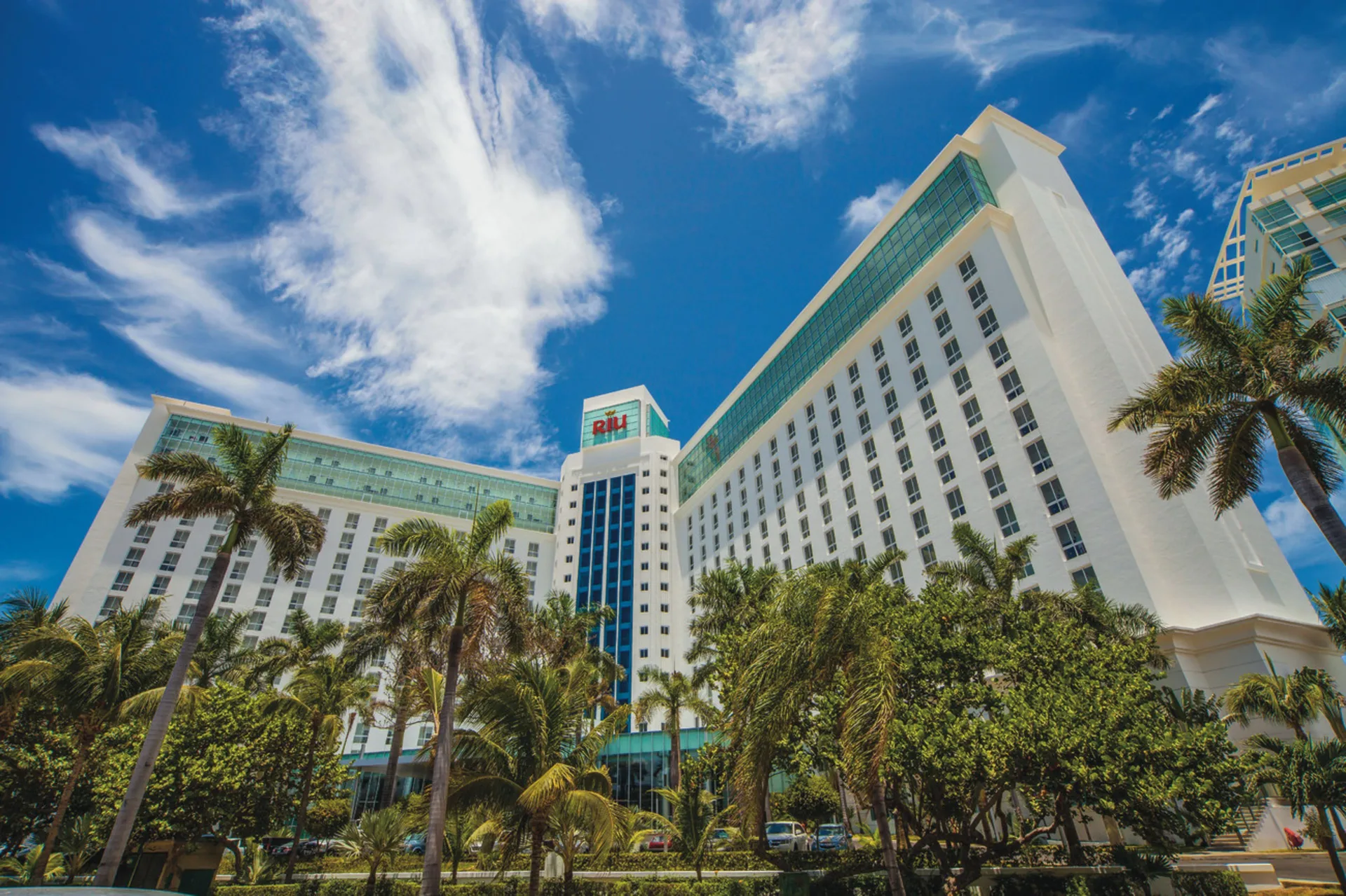 Palm-framed exterior towers of Hotel Riu Cancun under a blue sky.