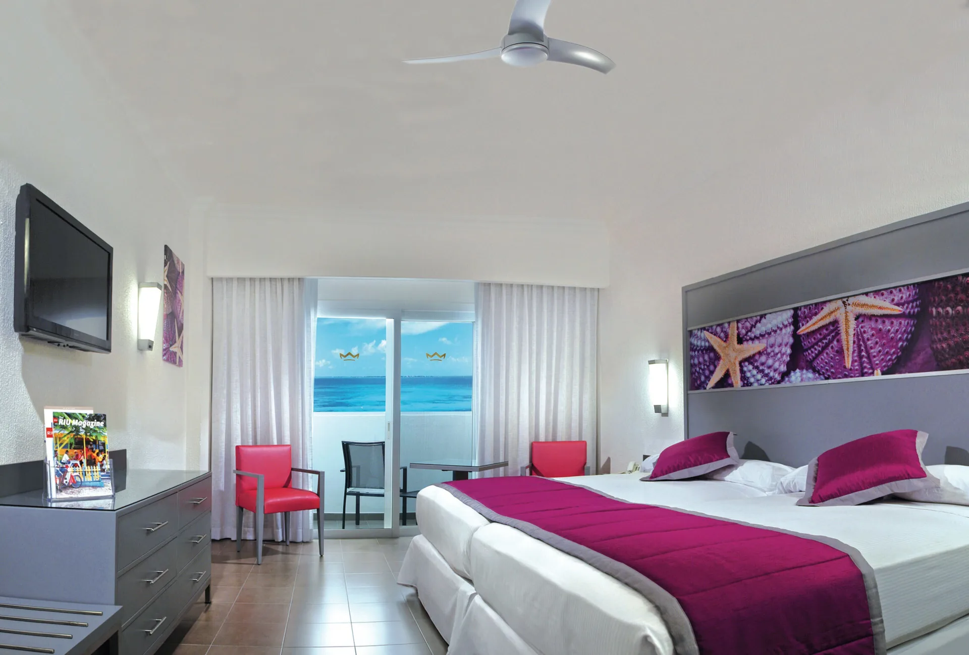 Guest room at Hotel Riu Cancun with two beds, magenta accents, and an ocean-facing balcony.