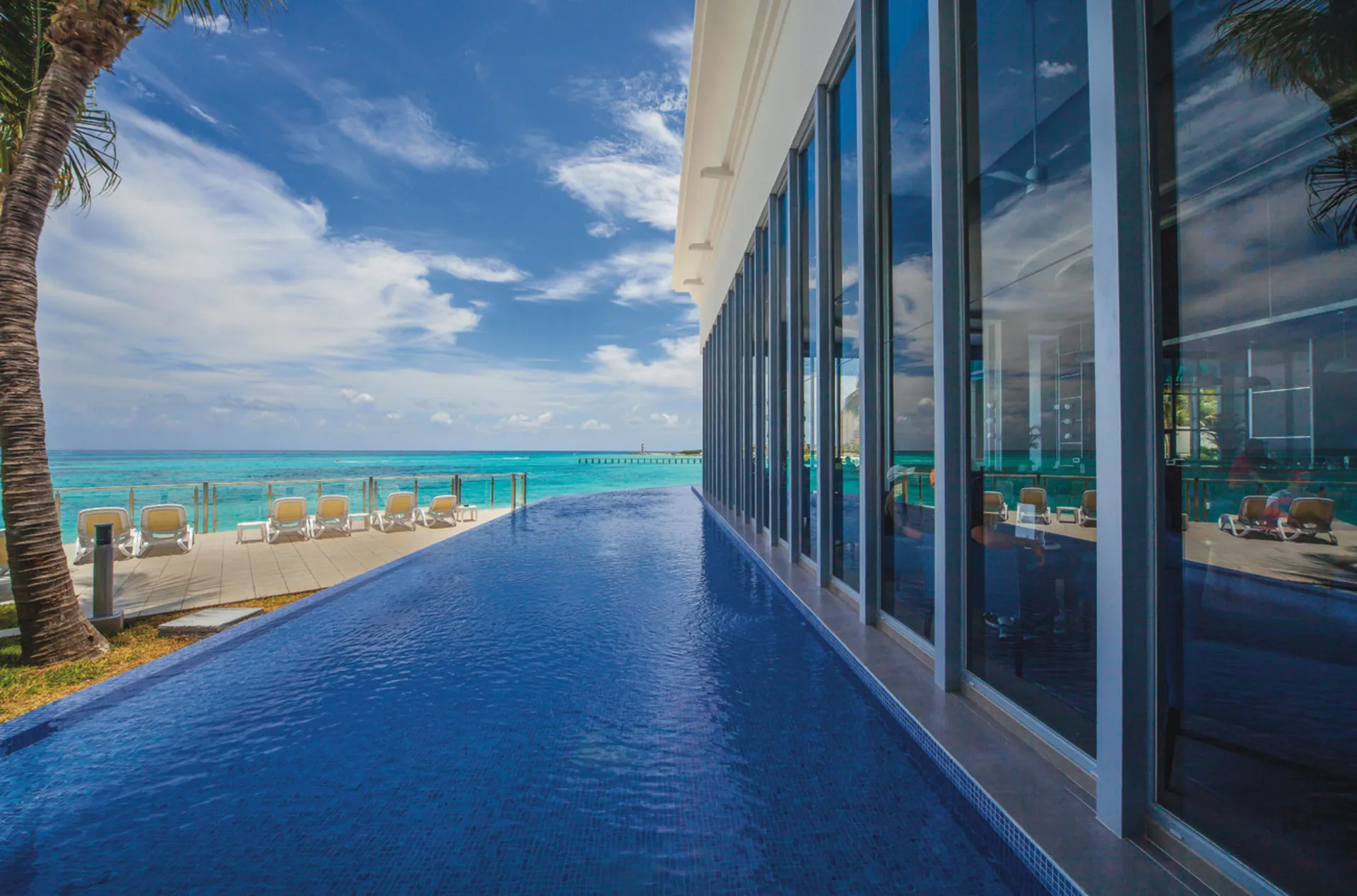 Infinity-edge pool at Hotel Riu Cancun beside glass walls and the turquoise sea.