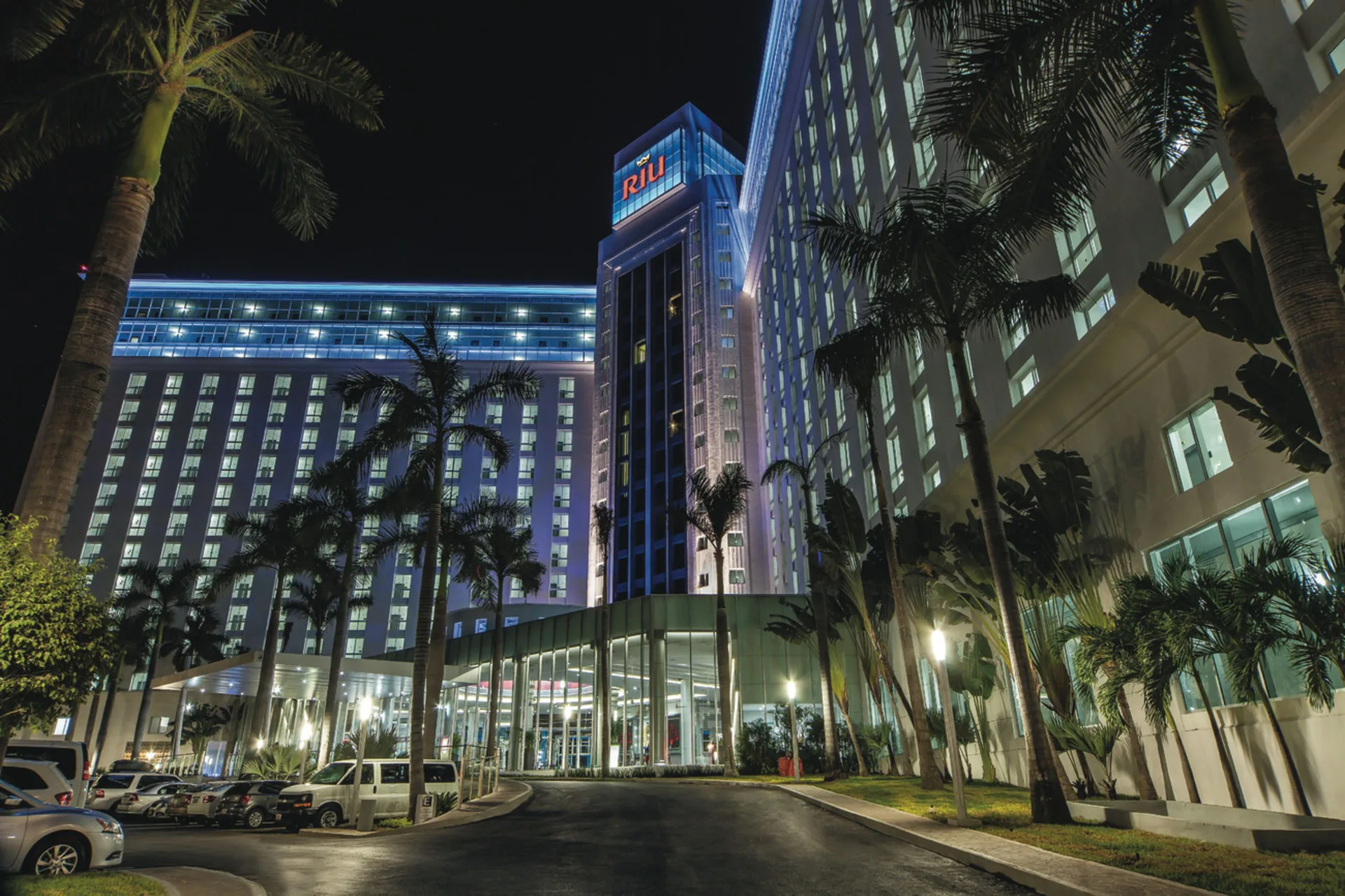 Hotel Riu Cancun exterior tower lit at night with palms in front.