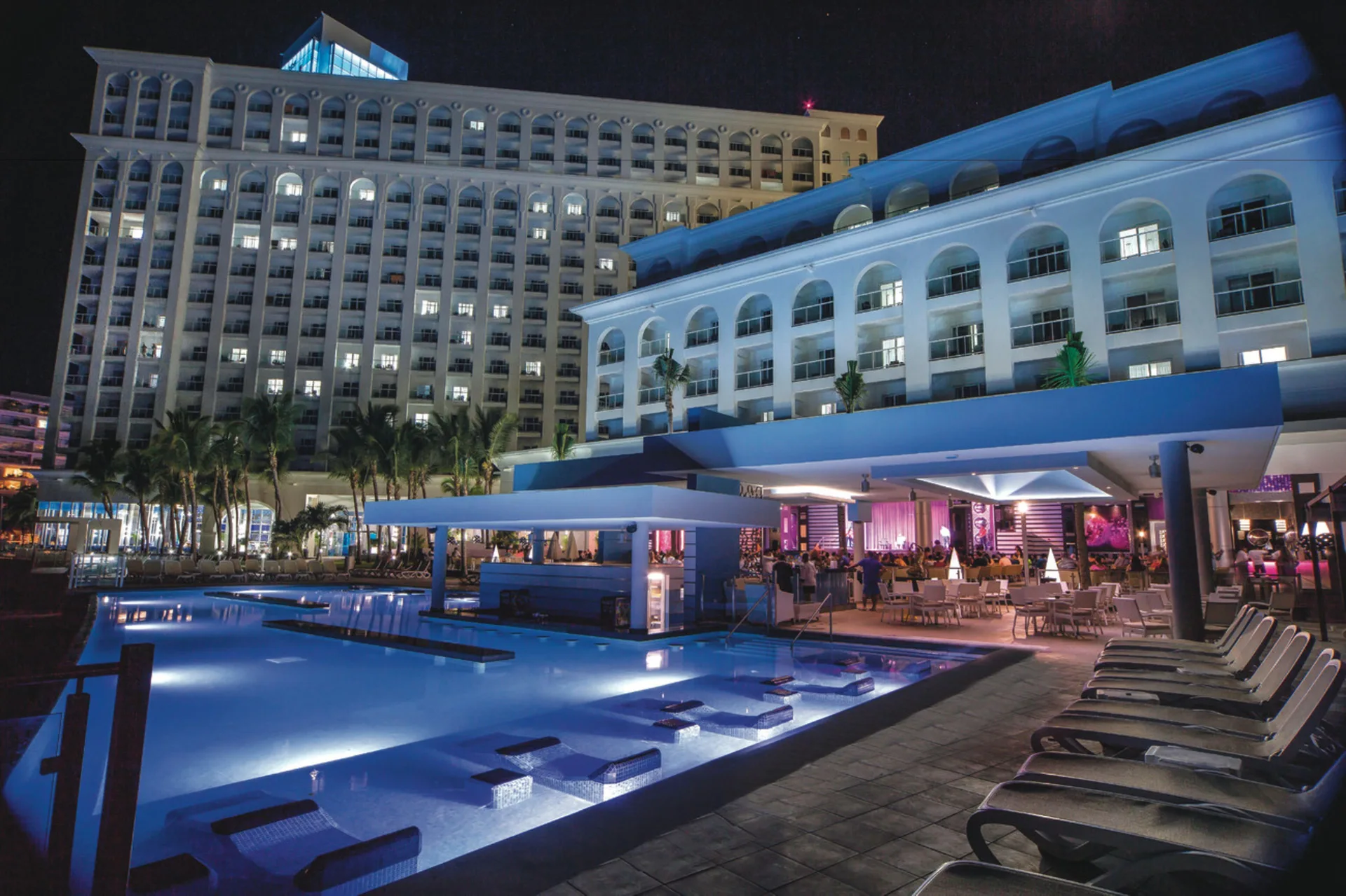 Illuminated pool deck and resort buildings at night at Hotel Riu Cancun.