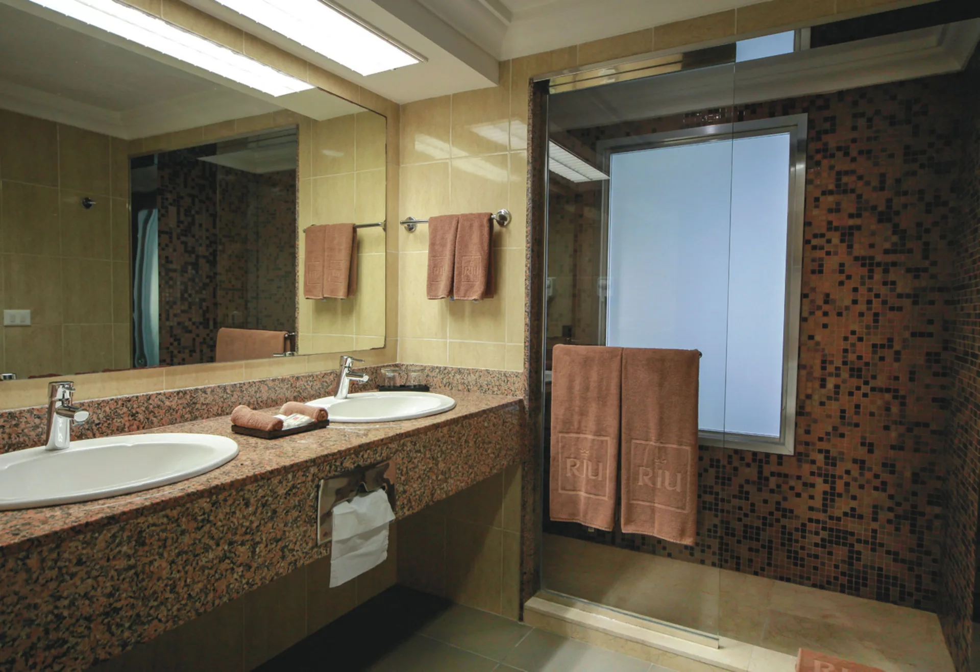 Junior Suite Ocean View bathroom with double sinks and glass shower at Hotel Riu Cancun.