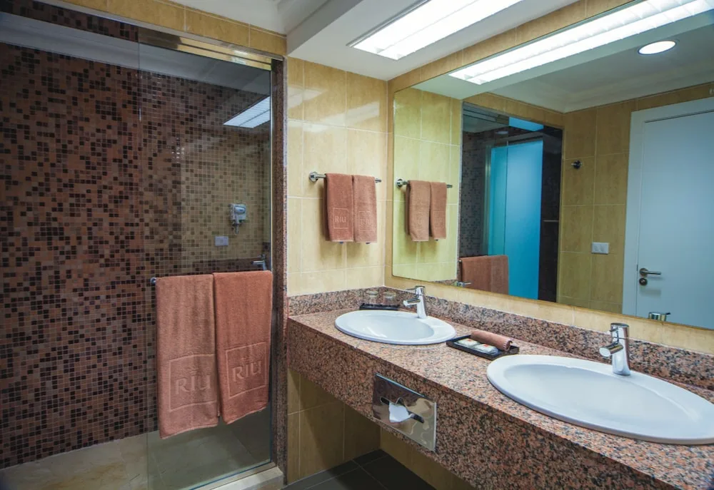 Guest bathroom with twin basins, mirror, and tiled shower at Hotel Riu Cancun.