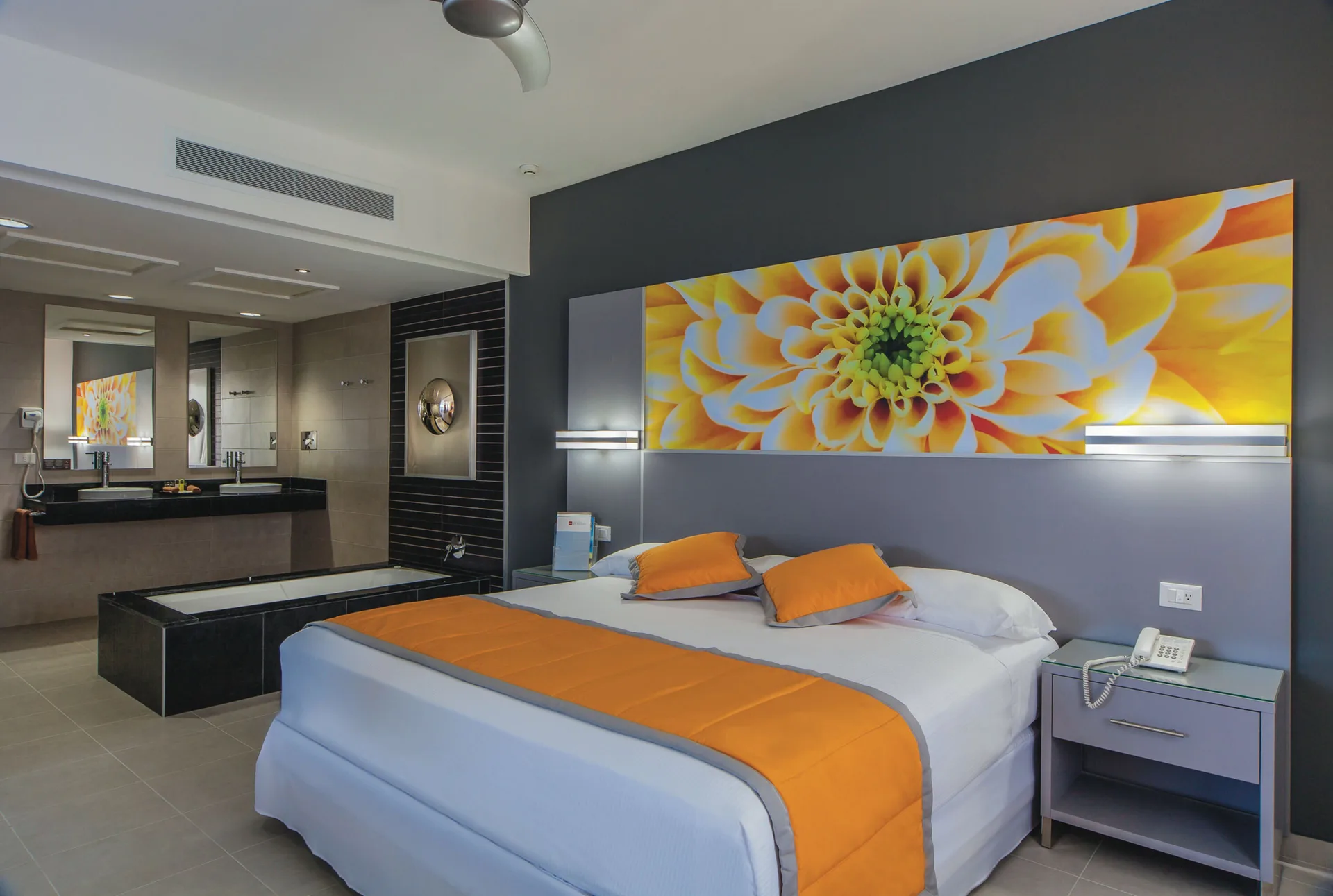 Suite Ocean View king bed with floral wall art and open bathroom at Hotel Riu Cancun.