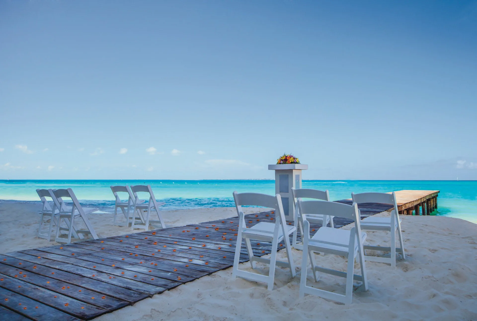 Beach wedding aisle with white chairs facing the sea at Hotel Riu Cancun.