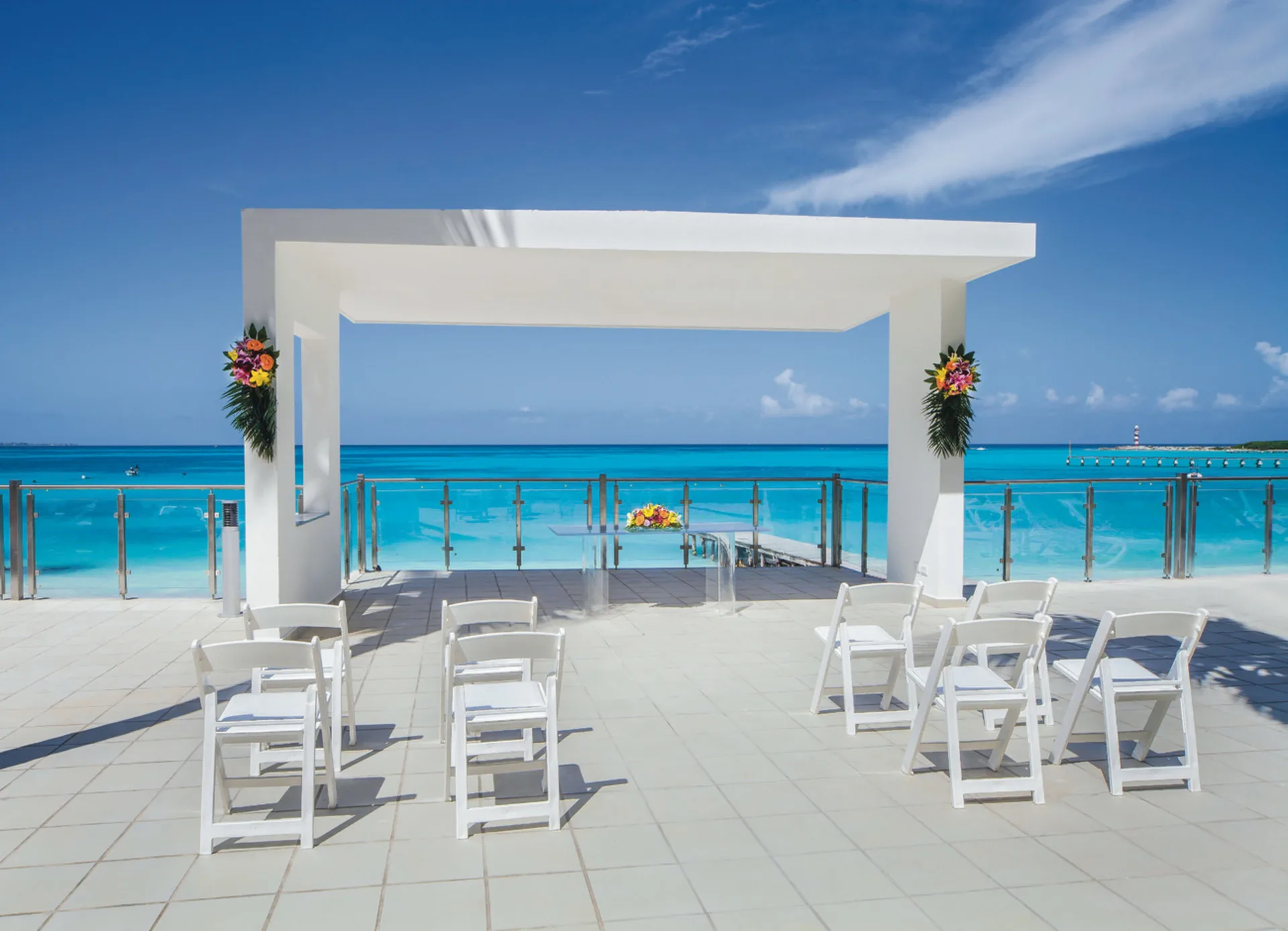 Oceanfront wedding arch with white chairs and flowers at Hotel Riu Cancun.