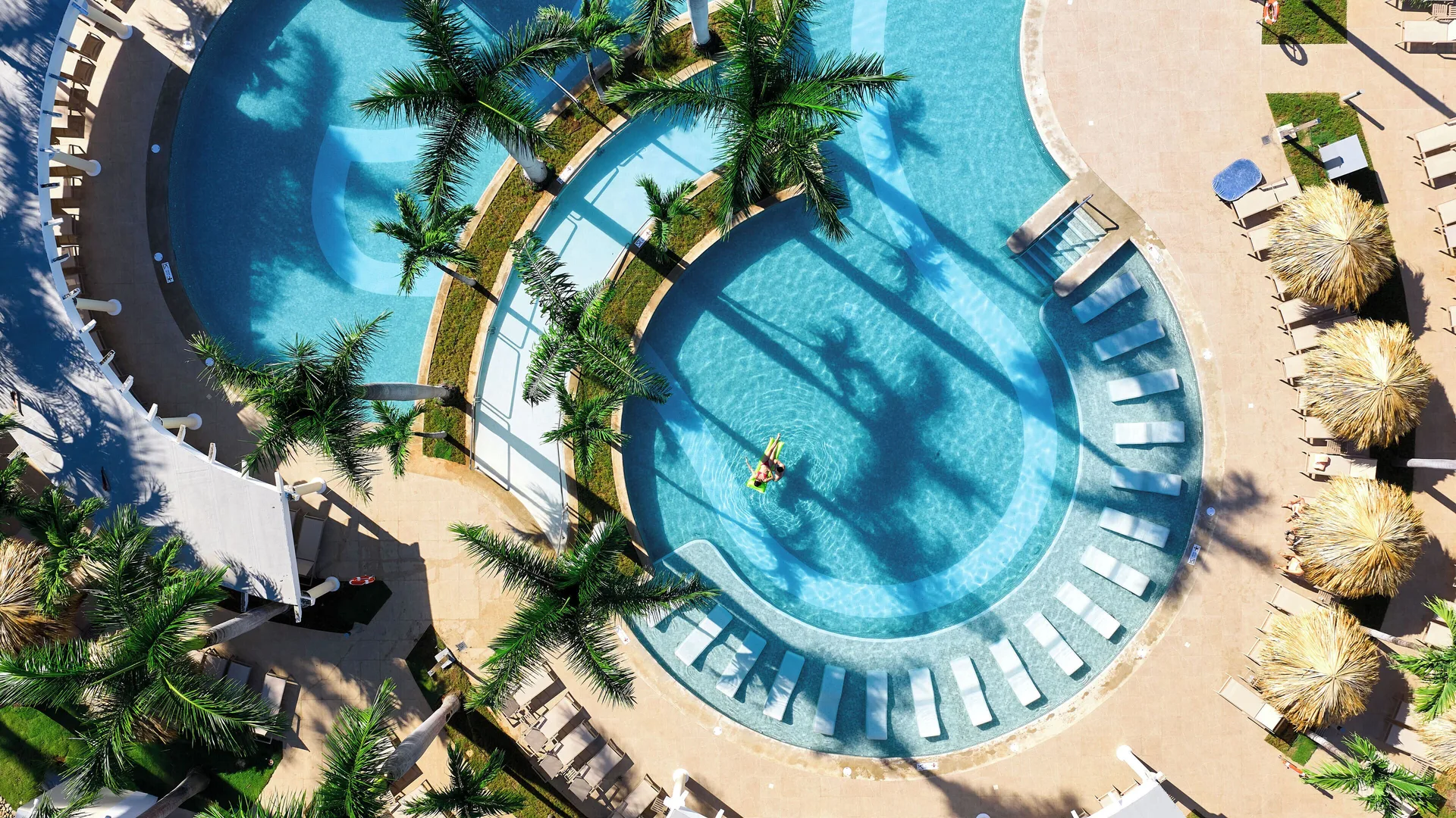 Aerial view of curved pools, palms, loungers and shaded palapas at Hotel Riu Guanacaste.